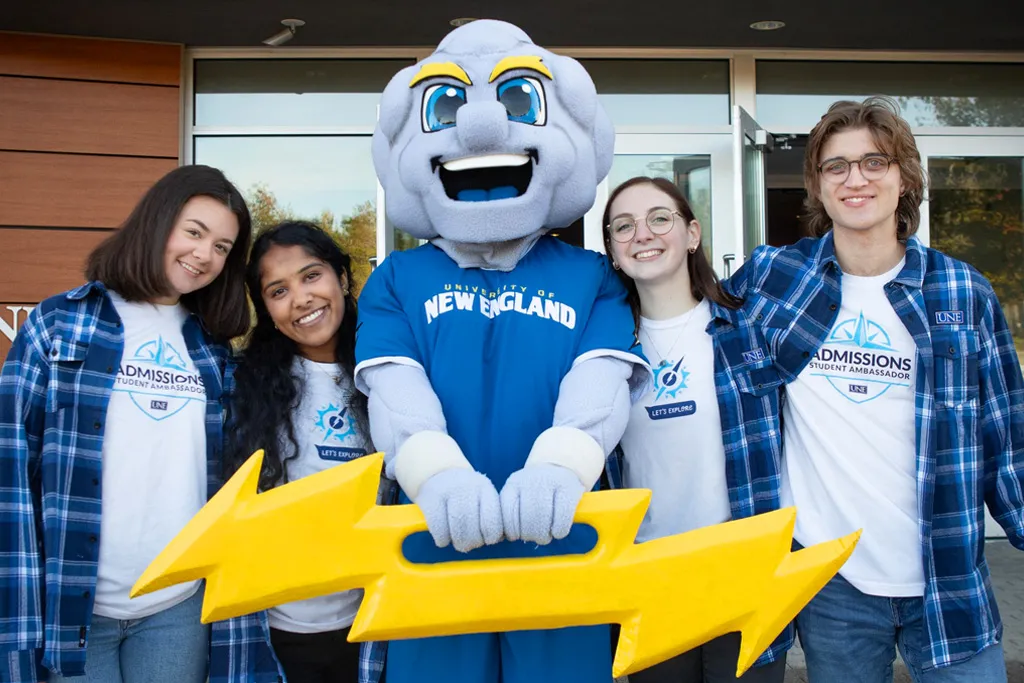 A group of four students wearing matching blue plaid flannels stand around Stormin' Norman