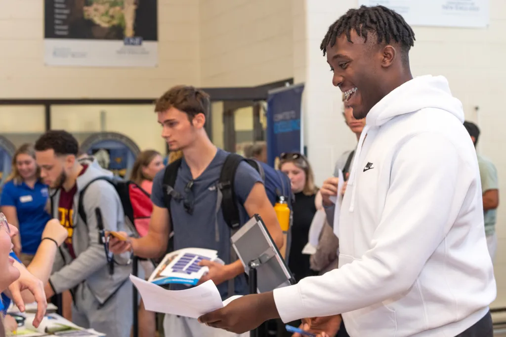 A new student happily passes orientation papers to a staff member