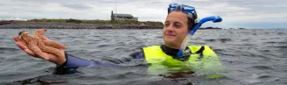 A student wearing snorkel gear holds up a starfish while in the ocean