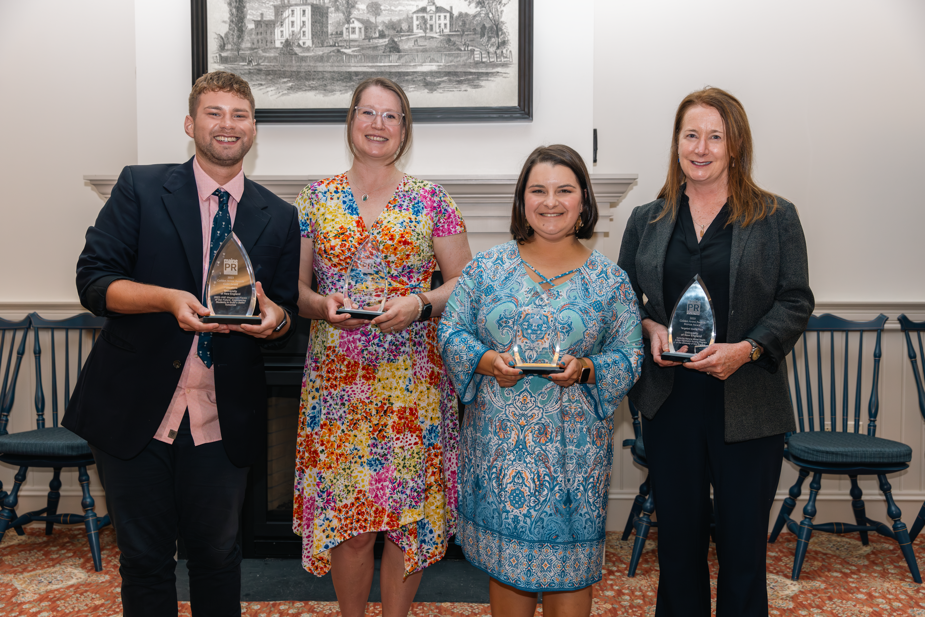 Four members of the Office of Communications pose for a photo in Alumni Hall holding awards