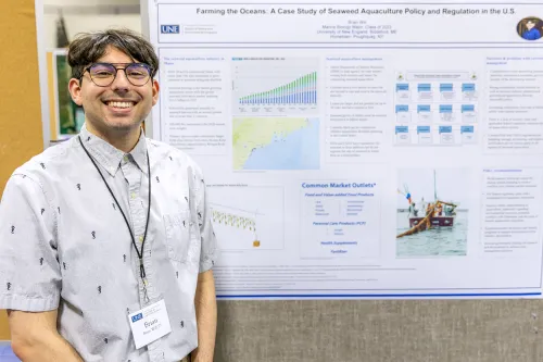 A student stands in front of their research poster titled, "Farming the Oceans: A Case Study of Seaweed Aquaculture Policy and Regulation in the U.S.”