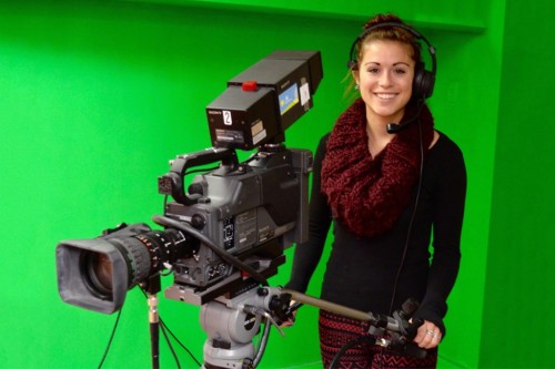 A student controls professional video equipment in front of a green screen