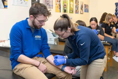 An athletic training student practices closing a wound on another student