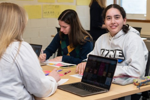 A student in a classroom of other students smiles at the camera