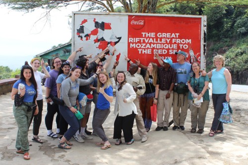 A group of students and others stand in front of a large sign with an illustrated map of Africa