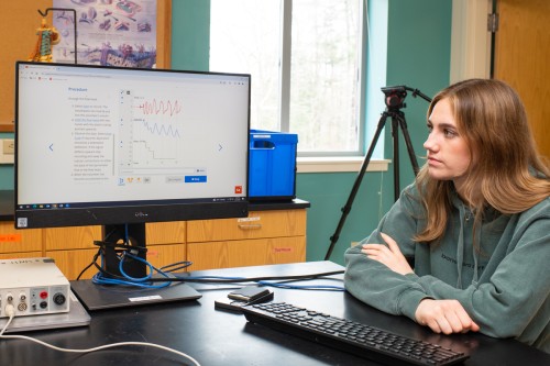 A student looks at a line graph with a red line, blue line, and green line on a monitor