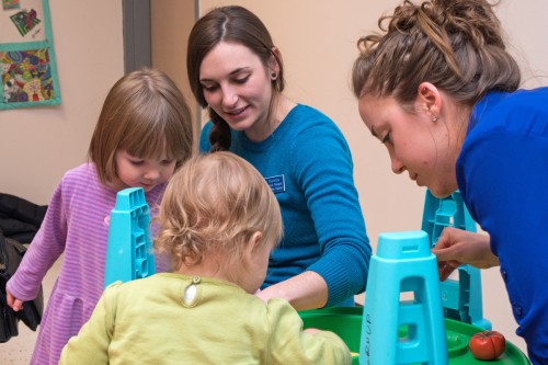 Two social work students playing in an indoor sandbox with two toddlers