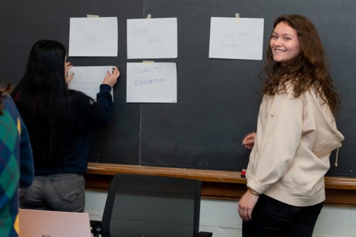 Two students place paper on a blackboard that describe aspects of education