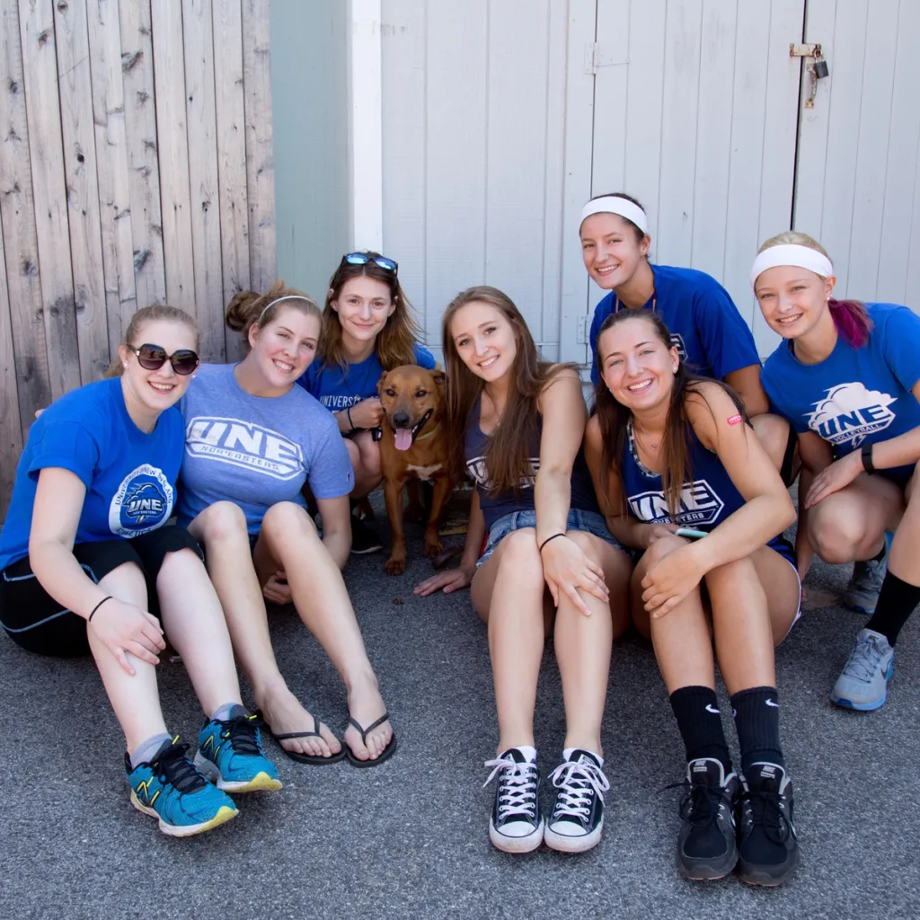 a group of students pose outside in matching blue u n e t-shirts with a dog