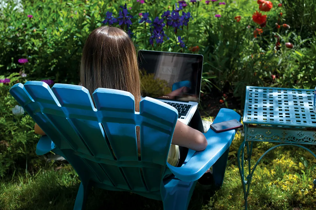 A U N E student types on a laptop while sitting outside