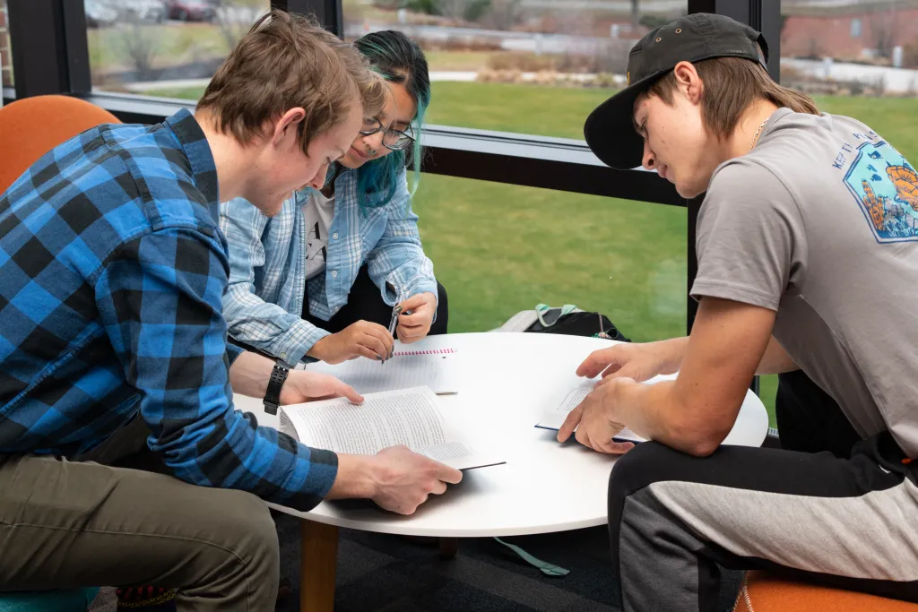 Three U N E students gather around a table studying notes