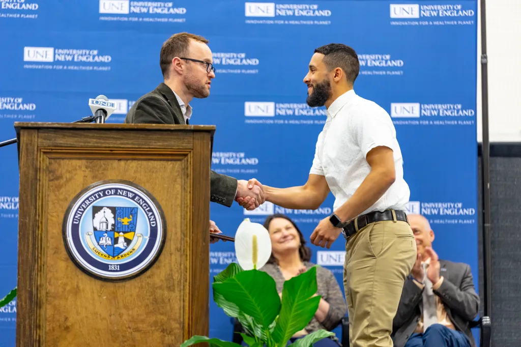 student in white shirt shaking hands on stage