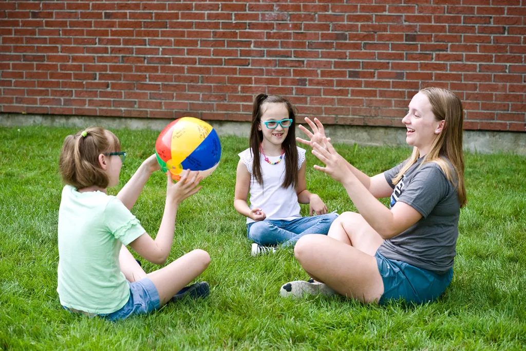 A special education student throws a beach ball outside with two elementary school children