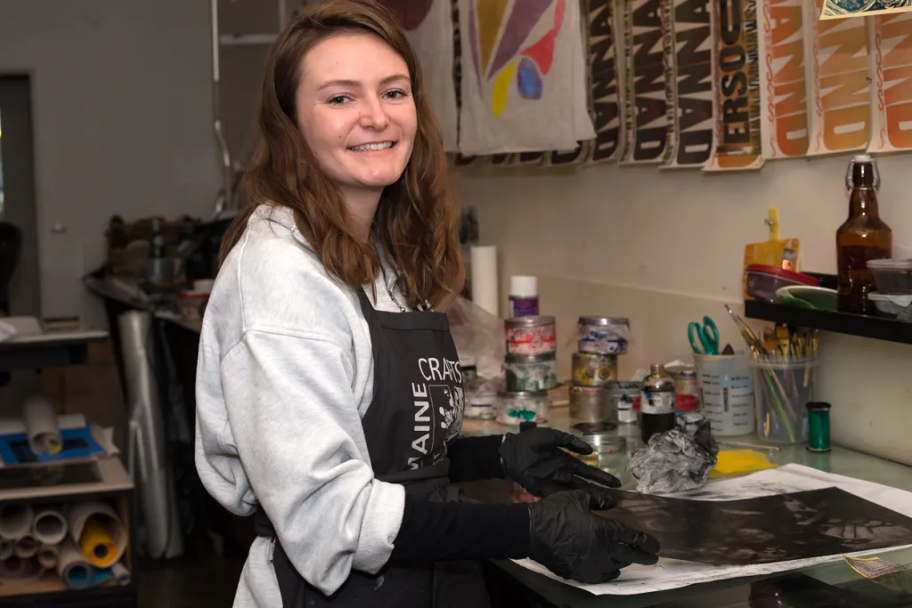 A student wears an apron and gloves while screenprinting at an internship