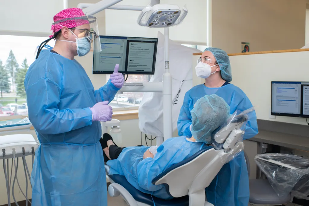 A dental student and a P A student in blue scrubs discuss dental work with a patient