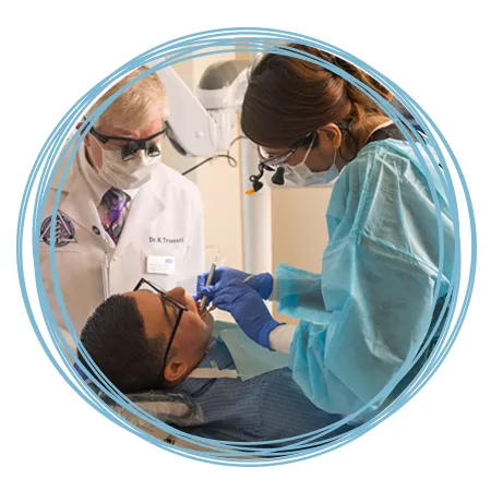 A dental student works on a patient's teeth while a professor reviews their technique