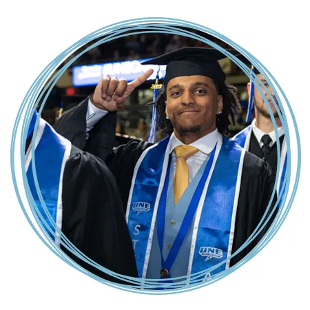 An undergraduate student in academic regalia smiles at their Commencement