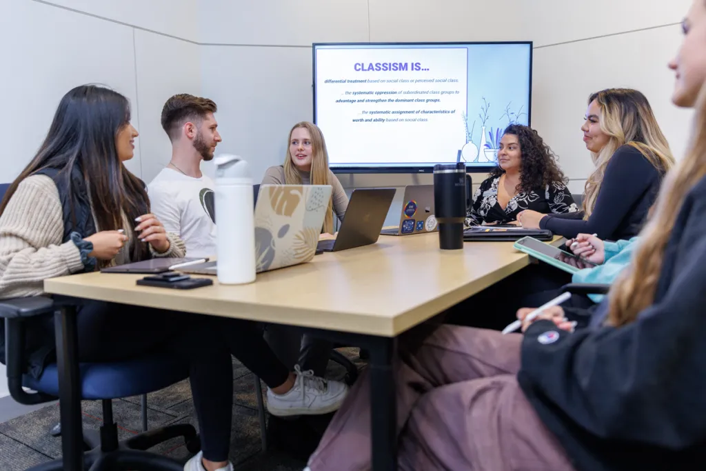 Six physical therapy students sit and talk in a study room