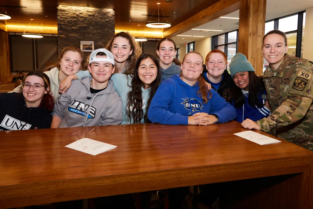 A group of U N E students smile with a veteran