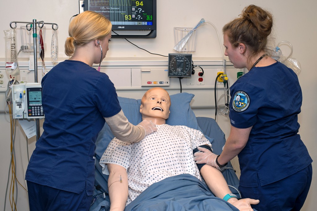 Two nursing students in their scrubs practice on a patient simulator in the Sim Lab