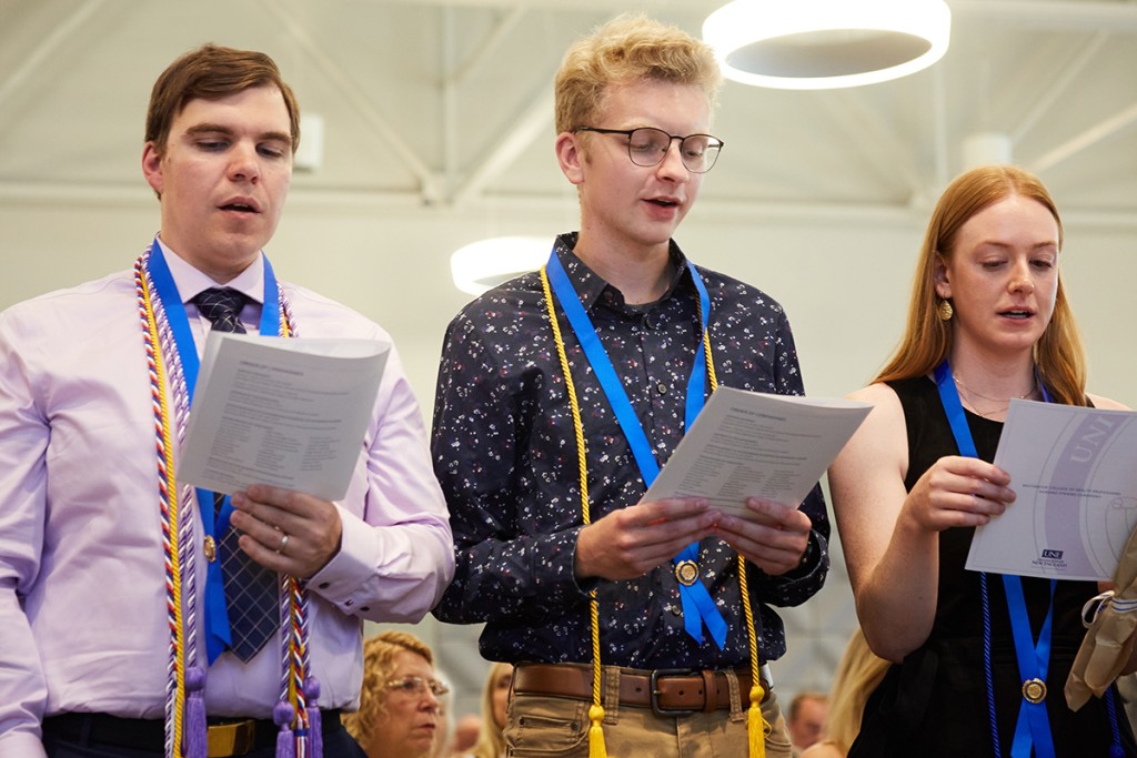 Three students wearing nursing cords hold up and recite the nursing pledge