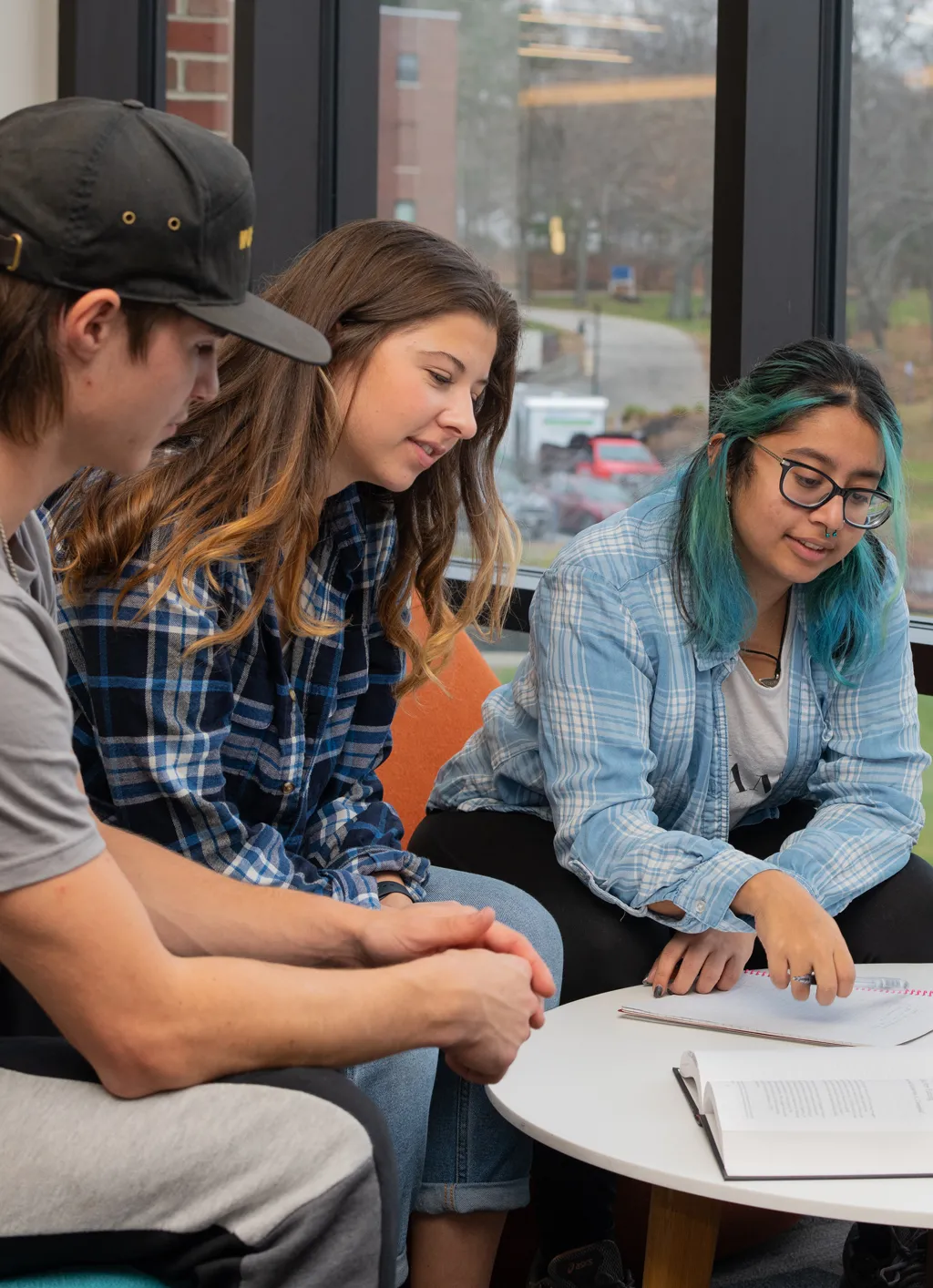 Three students sit at a table and read class notes off a notebook