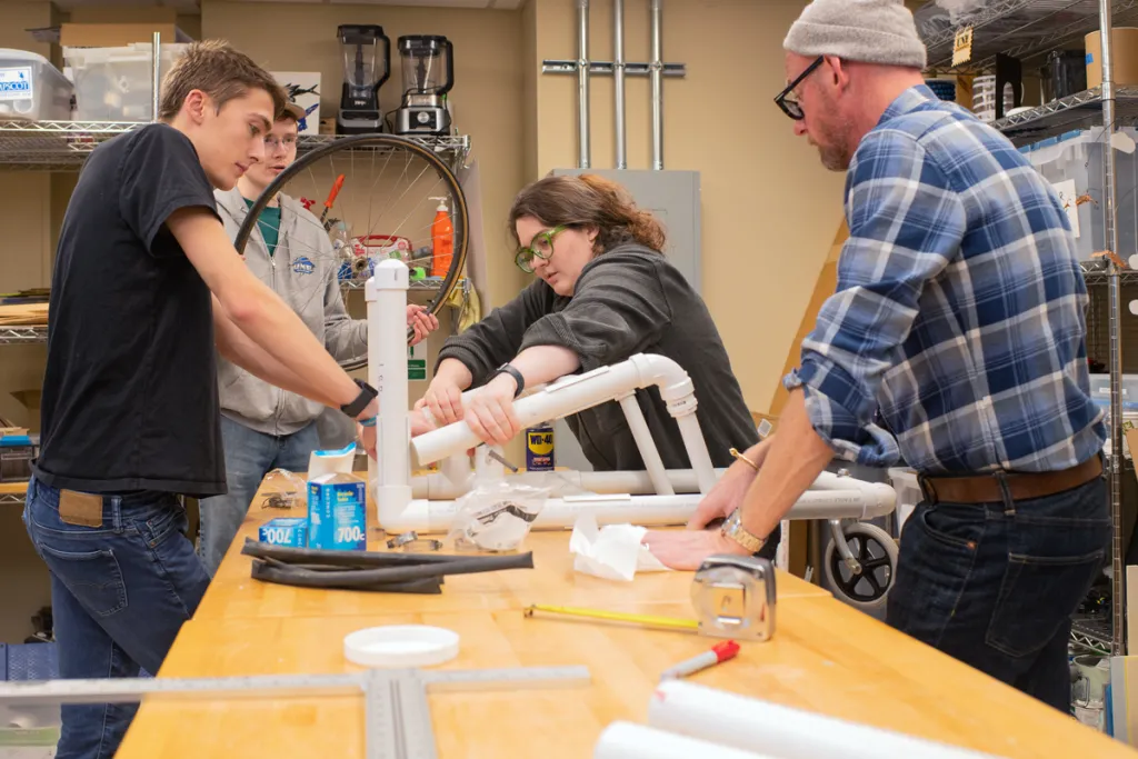 Three students and a professor assemble part of a wheelchair together