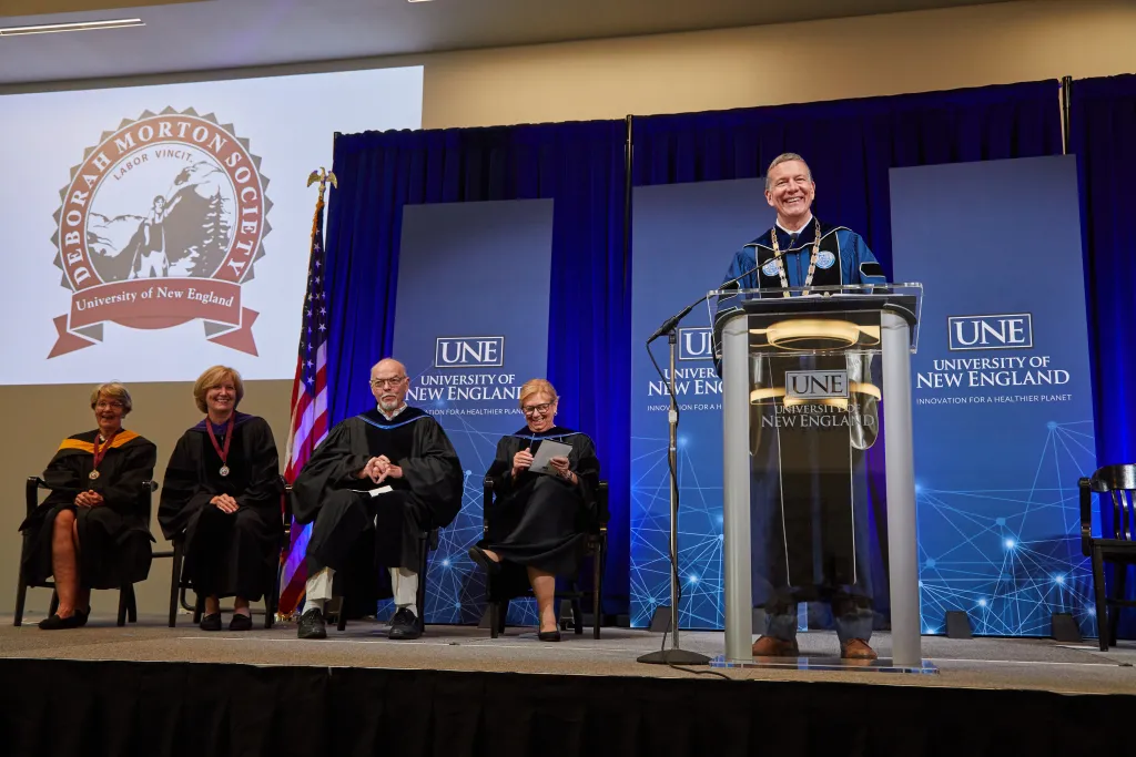 UNE President James Herbert speaks at a podium in regalia