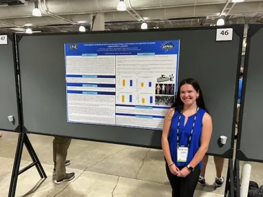 A UNE student poses in front of a research poster