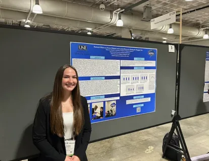 A UNE student poses in front of a research poster