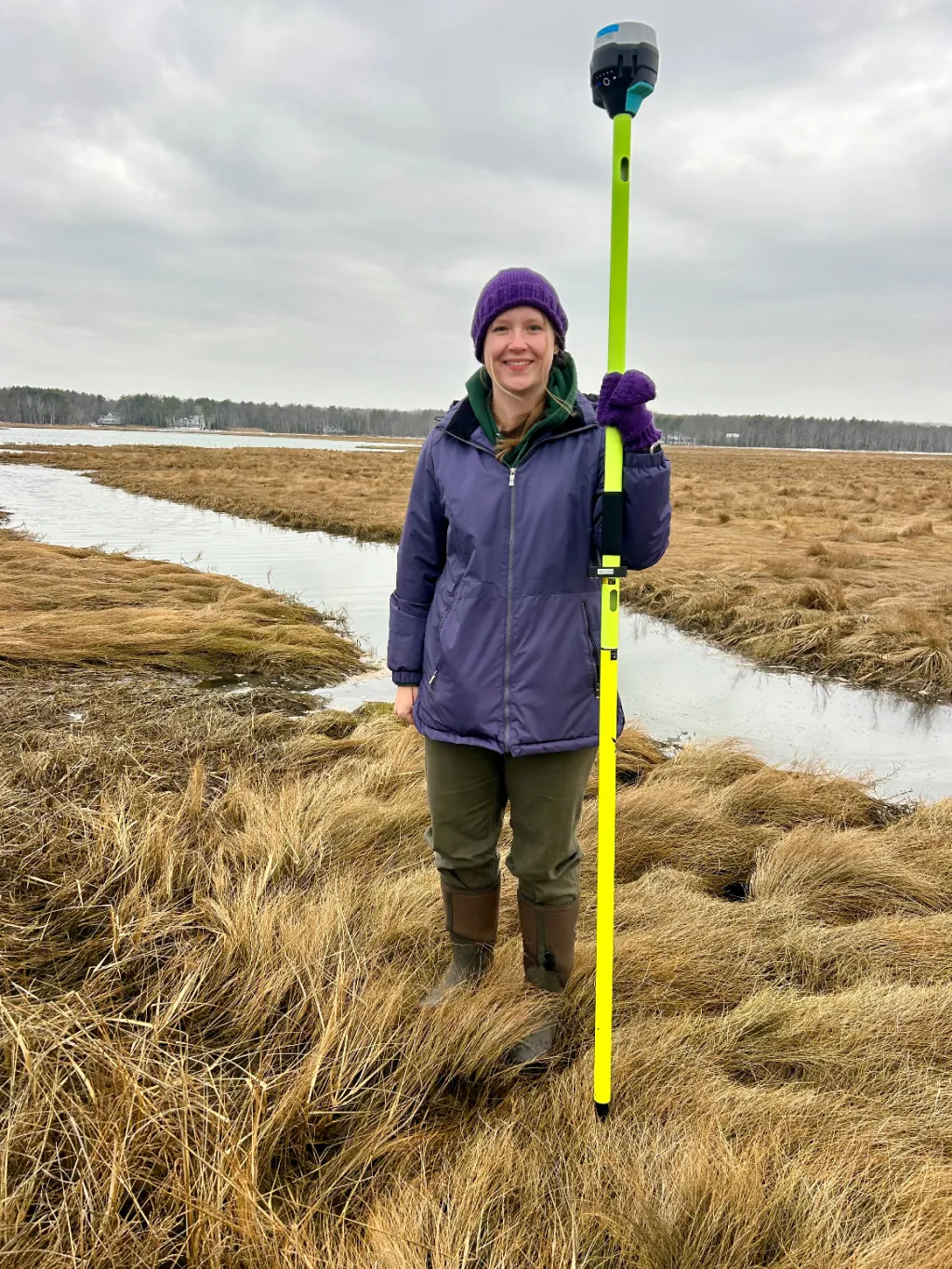 Katelyn DeWater holds land survey equipment in the Biddeford Pool salt marshes