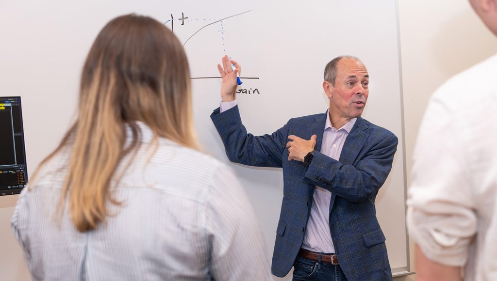 A professor explains a graph on a whiteboard