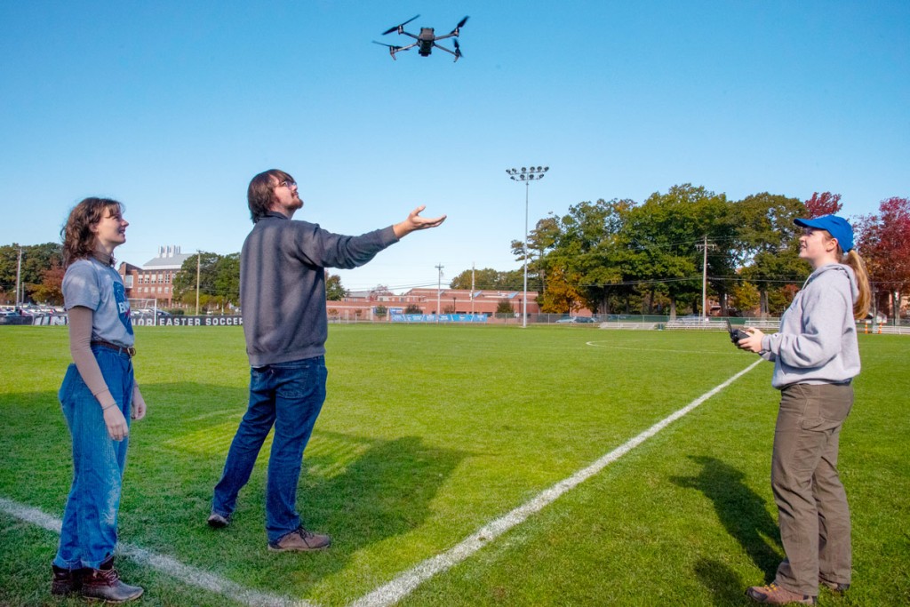 Three students flying a drone from a soccer field