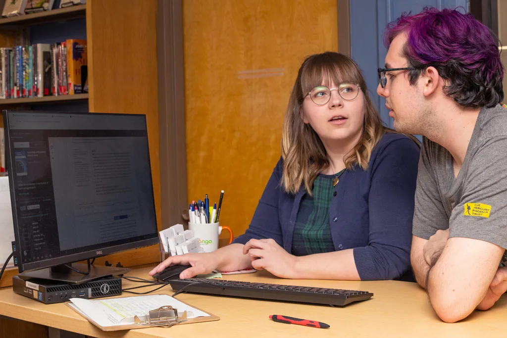 A student looks up research articles on a computer with the U N E librarian