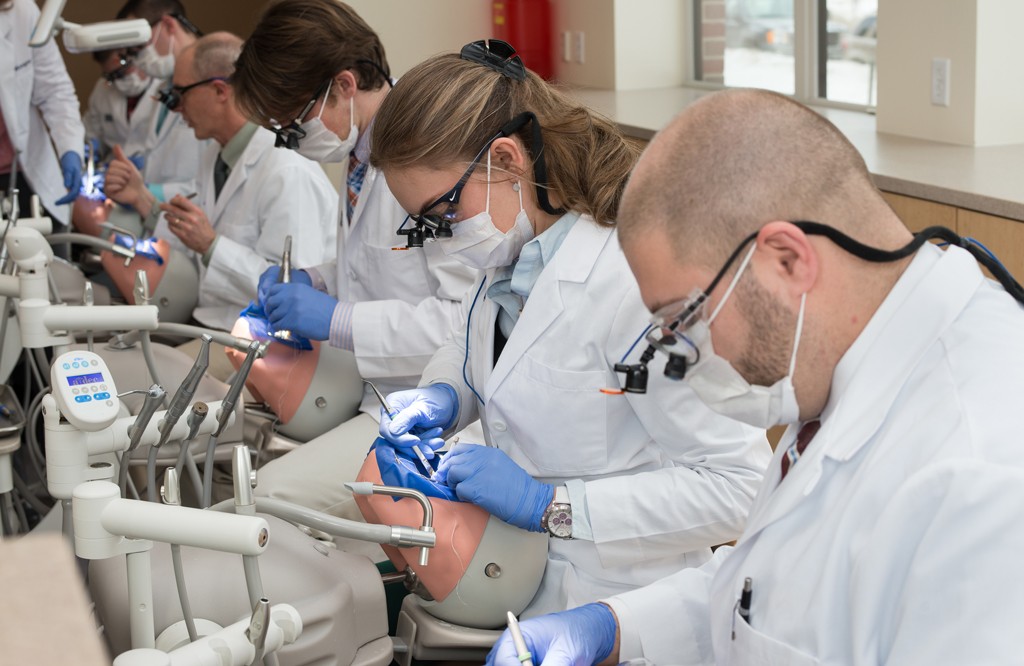 A row of dental students practicing teeth cleaning on patient simulators