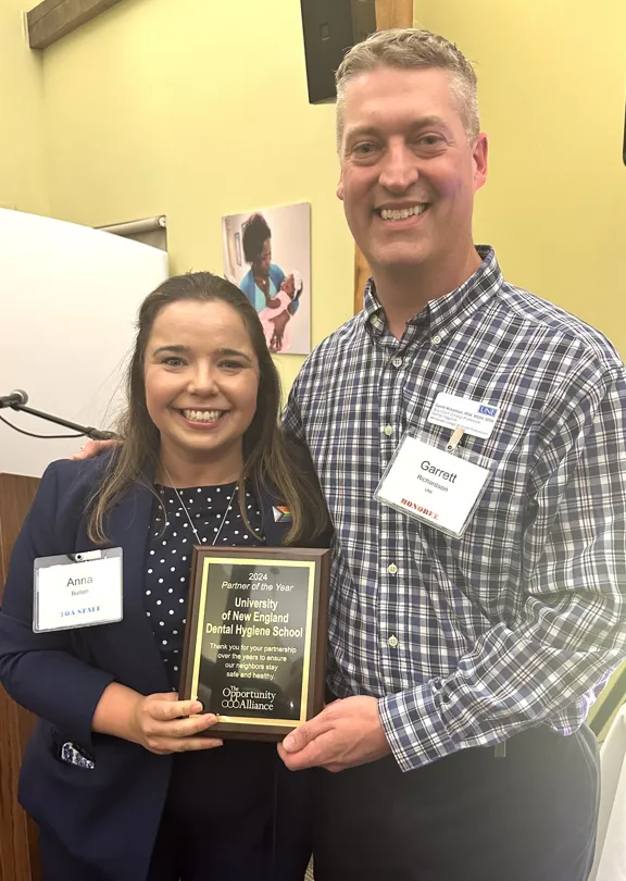 A UNE professor and social worker pose with an award plaque 