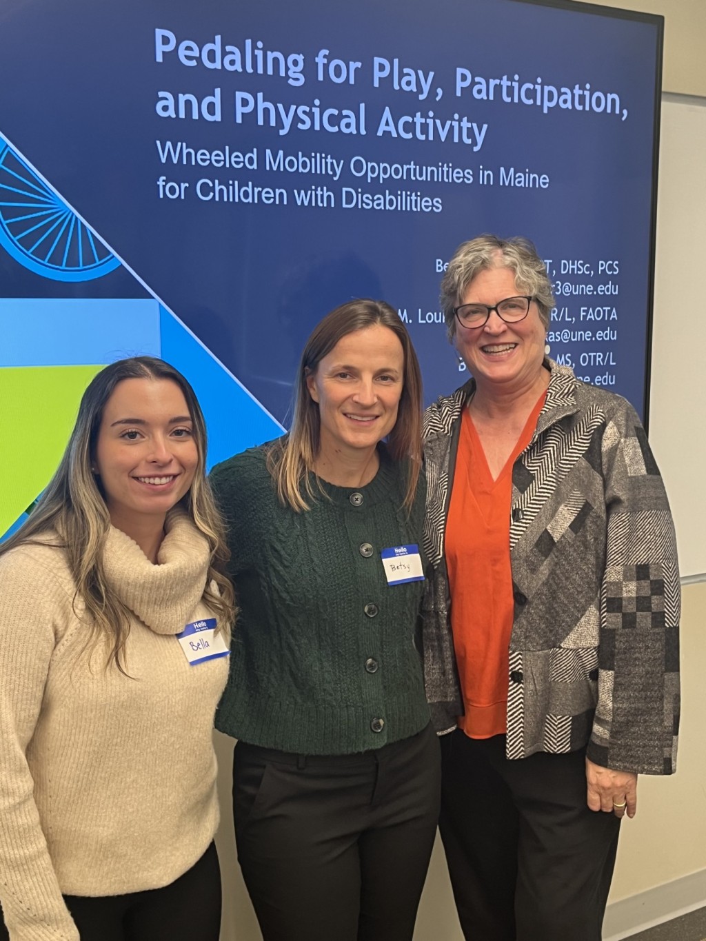 Three members of the UNE OT program pose in front of a presentation