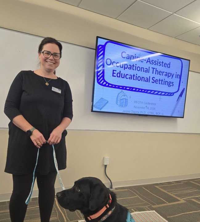 A woman poses with a therapy dog in a classroom