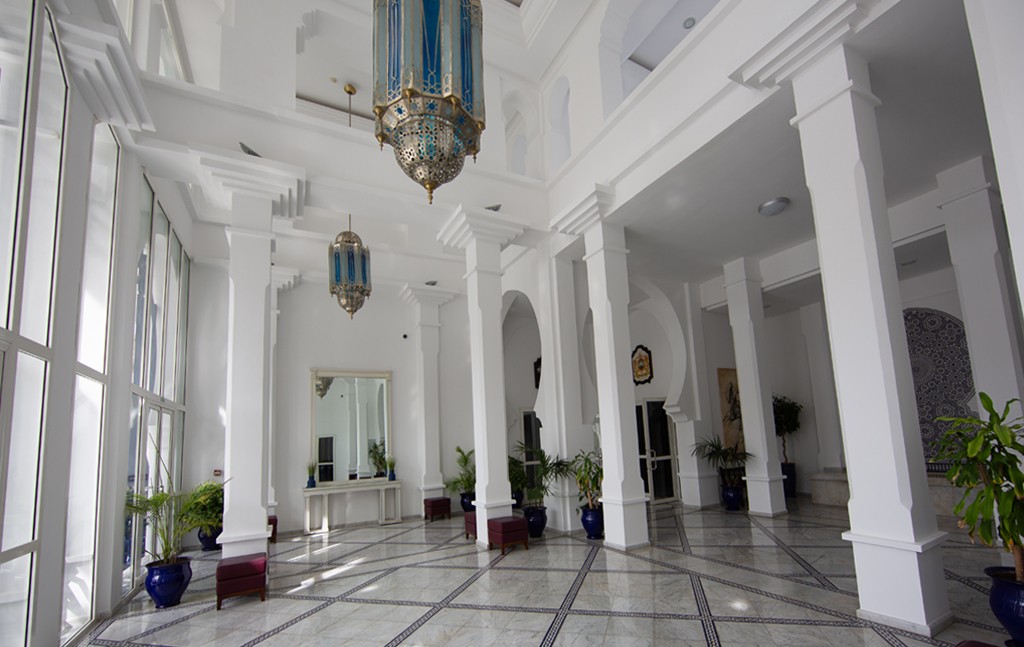 An interior room with white columns and blue and silver Moroccan lamps hanging from the ceiling