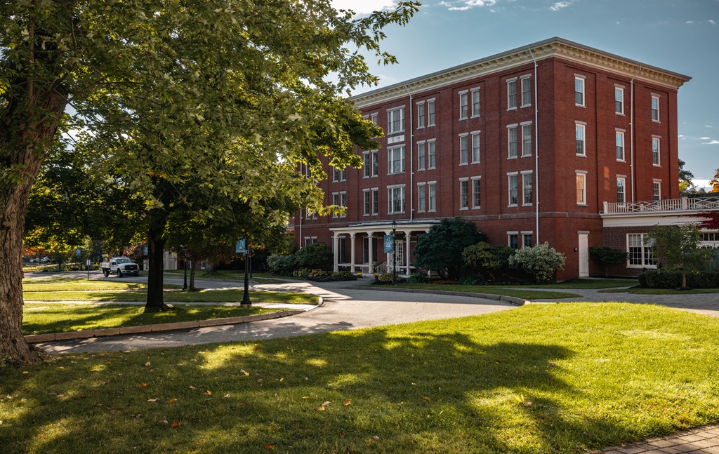 A brick building sits behind green grass and a large tree