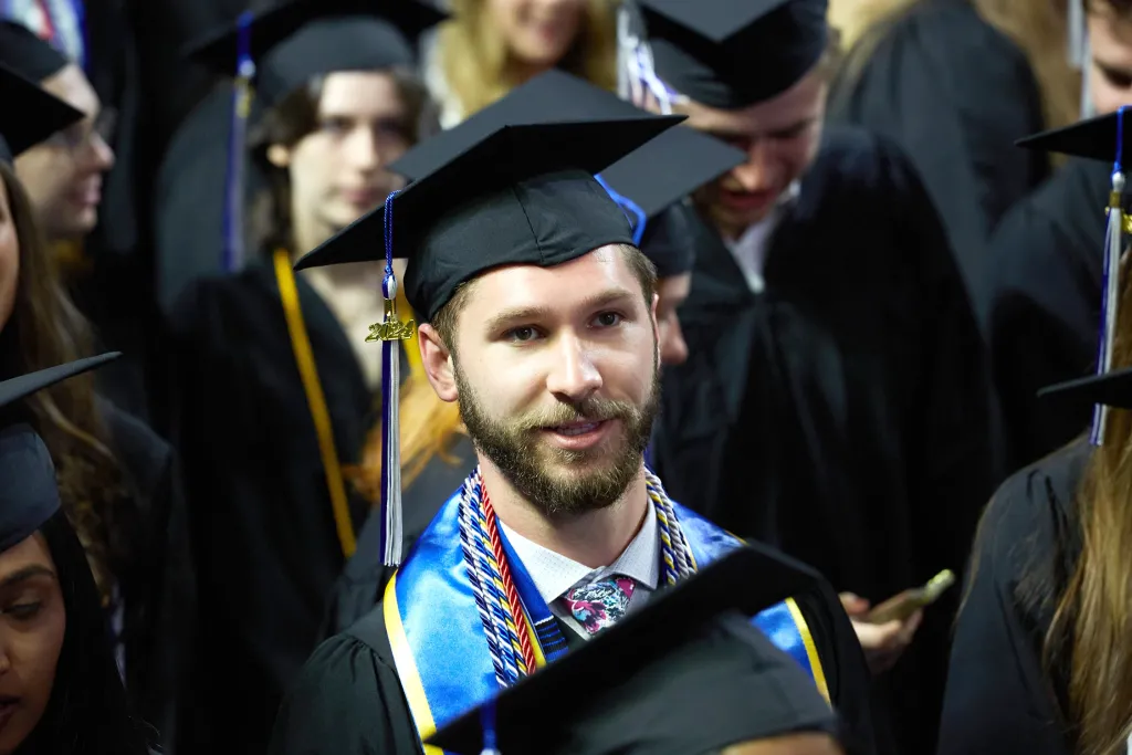 A U N E graduate student standing in the crowd of students waiting to cross the stage at commemcement 