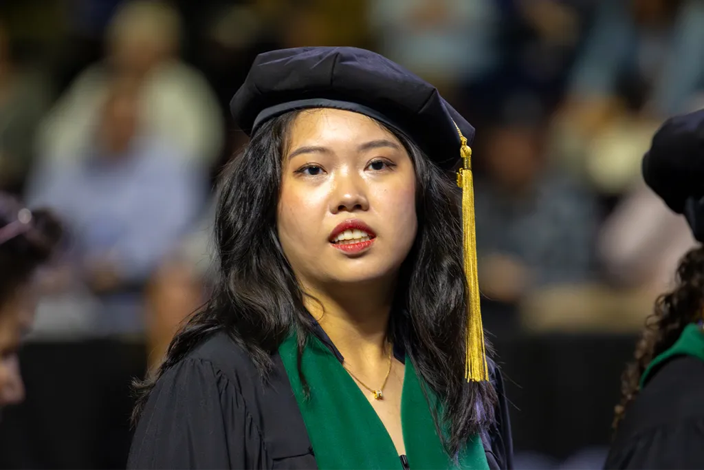 A U N E graduate student in her regalia while looking to the stage