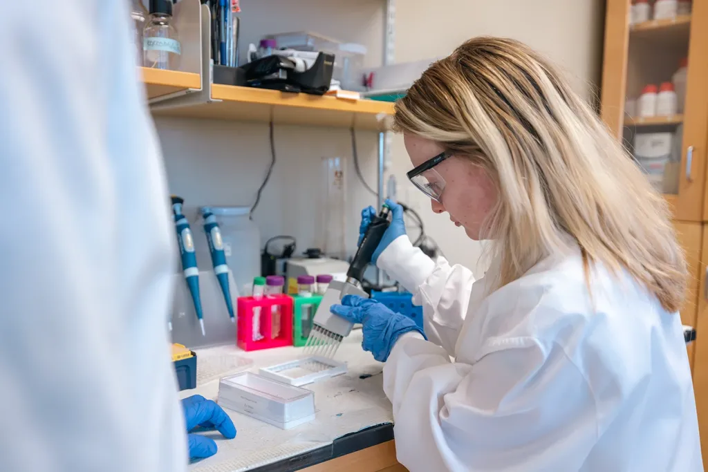 A female U N E student pipetting samples in Sri Mohan's research lab