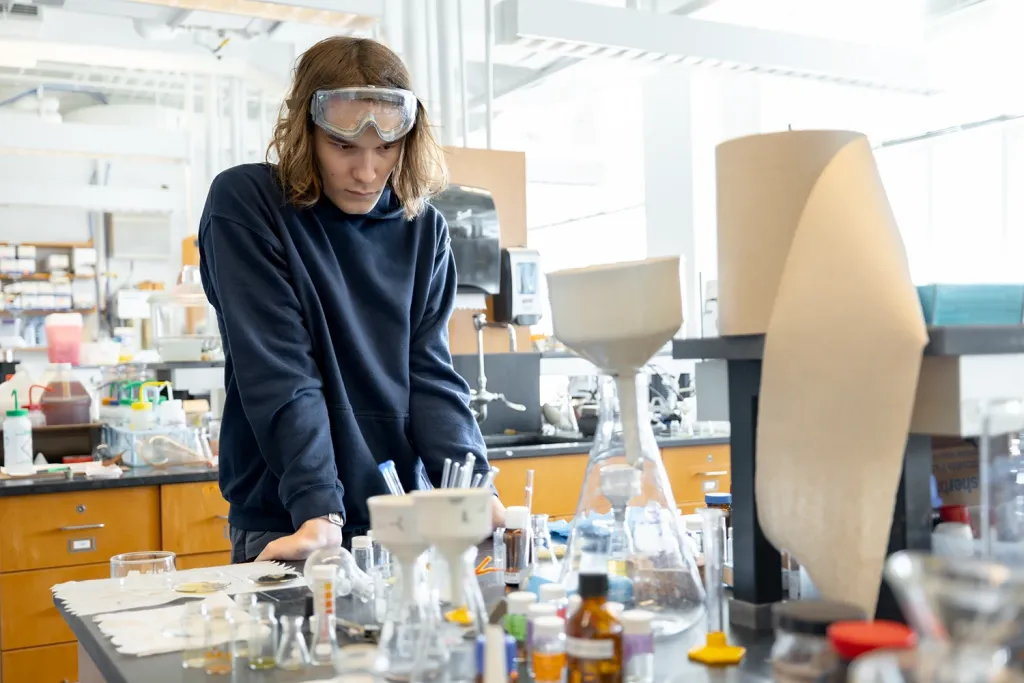 A U N E student stands and stares at a beakers and samples in a lab