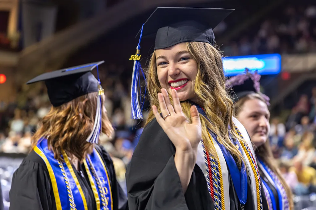 A U N E graduate smiles and waves at the camera