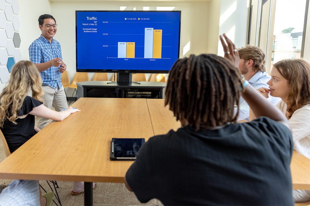 One UNE student presents to a groups of business students and one raises a hand to ask a question