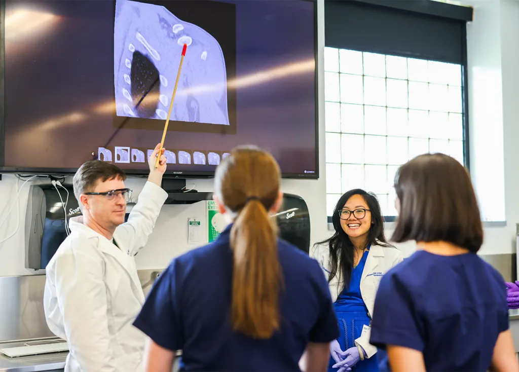 A group of clinical anatomy students review an anatomical image on a large monitor