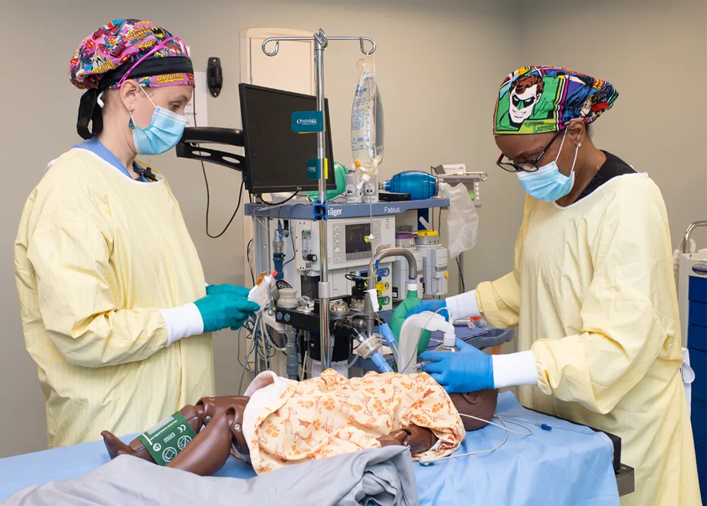 Two D.N.P. students practice giving anesthesia to a child patient simulator