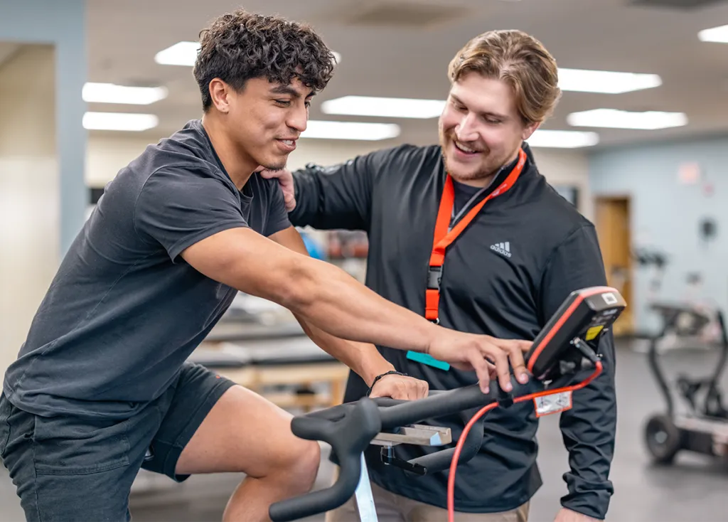 A D.P.T. student supports a patient riding a stationary bike