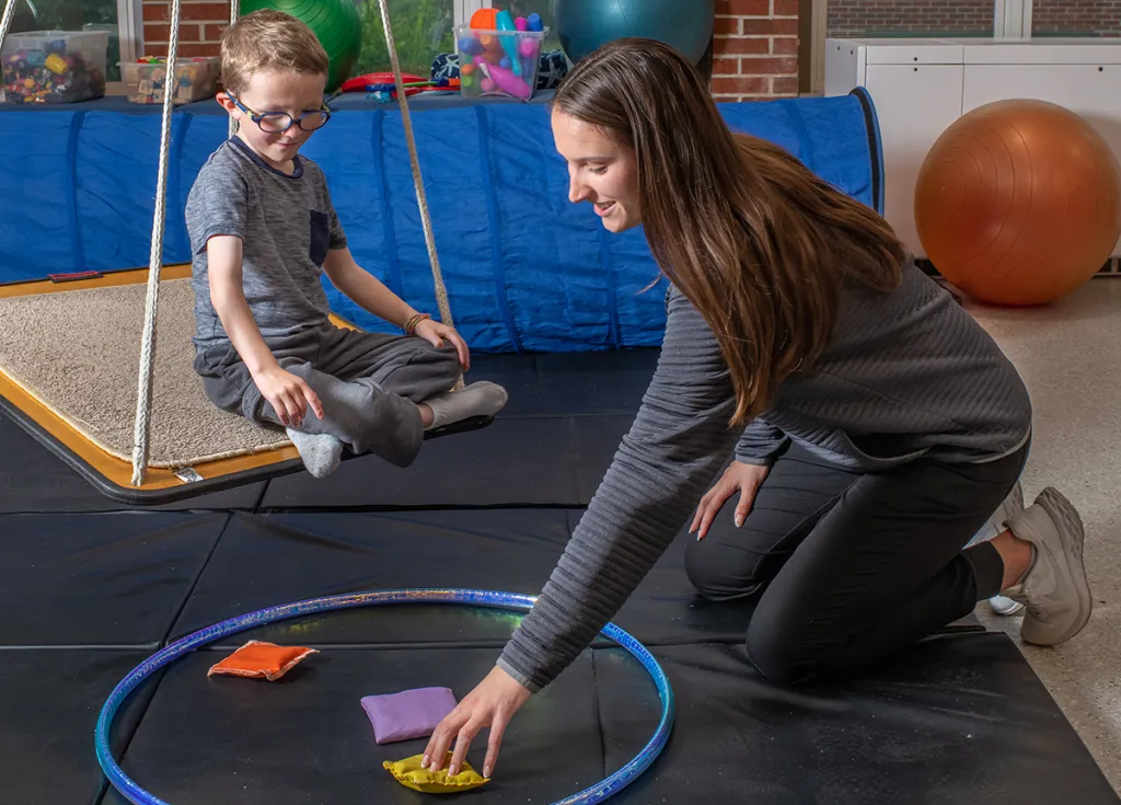 An M S O T student reaches down for a small bean bag to give to a child sitting on a swing